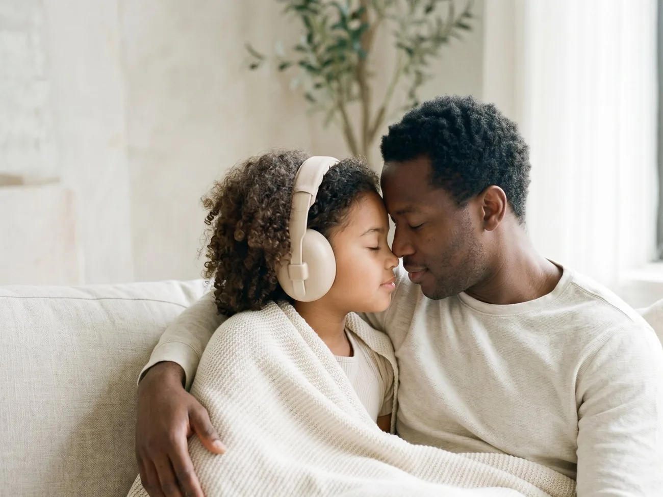 A father and his young daughter resting their heads together, the daughter wearing headphones, calm and close.
